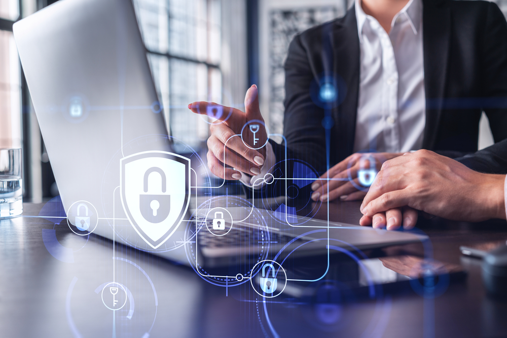 Two business people working on the project to protect cyber security of international company using laptop. Padlock Hologram icons. Teamwork concept. Understanding CMMC Level 2 Compliance